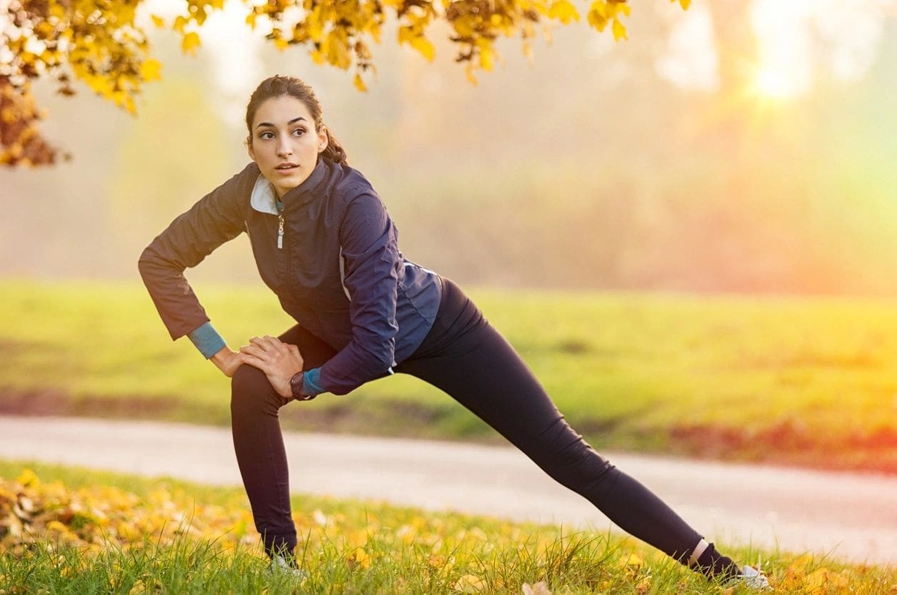 A woman stretching in the grass near a tree.