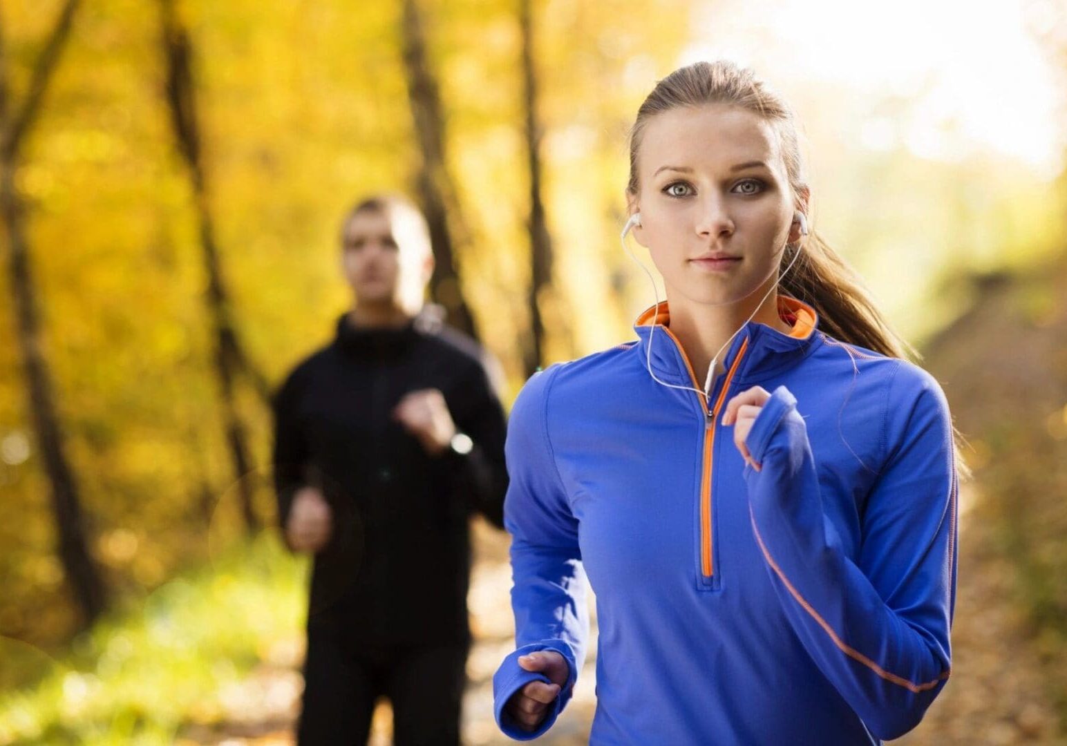 A woman running in the woods while wearing headphones.