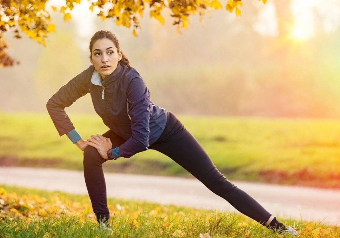 A woman stretching in the grass near a tree.